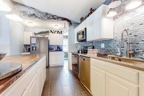 A modern kitchen with white cabinetry, a tiled backsplash, and stainless steel appliances. - Dog-friendly home 5 blocks from the beach with patio, fireplace & prime location (Ocean City)