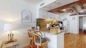 A kitchen with white cabinets, a central island, a dining area with wicker chairs, and a small table with a lamp. - Dog-friendly 1st-floor end condo with beach entrance view - steps to the beach (Ocean City)