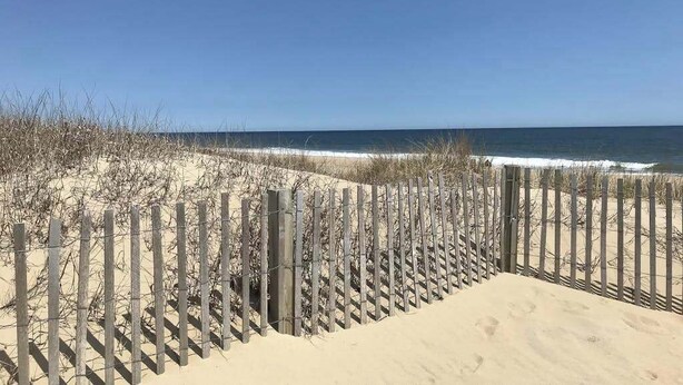 A sandy beach with a wooden fence and sparse vegetation. - Dog-friendly 1st-floor end condo with beach entrance view - steps to the beach (Ocean City)
