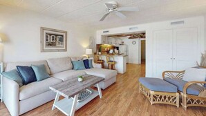A living room with a sofa, coffee table, and wicker chairs. There is a kitchen area with cabinets and a microwave. - Dog-friendly 1st-floor end condo with beach entrance view - steps to the beach (Ocean City)