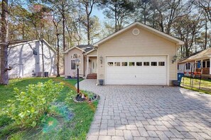 A single-story house with a garage, surrounded by trees and a well-maintained lawn. - Trinity Place Treasure (Ocean Pines)