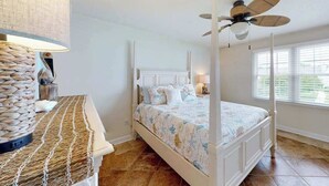 Ein Schlafzimmer mit einem Himmelbett, einem Deckenventilator und einem großen Fenster mit Jalousien.