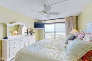 Ein Schlafzimmer mit Bett, Kommode, Deckenventilator, großem Fenster und Meerblick.