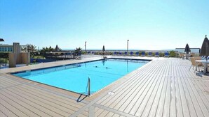 En swimmingpool med træterrasse, liggestole og havudsigt.