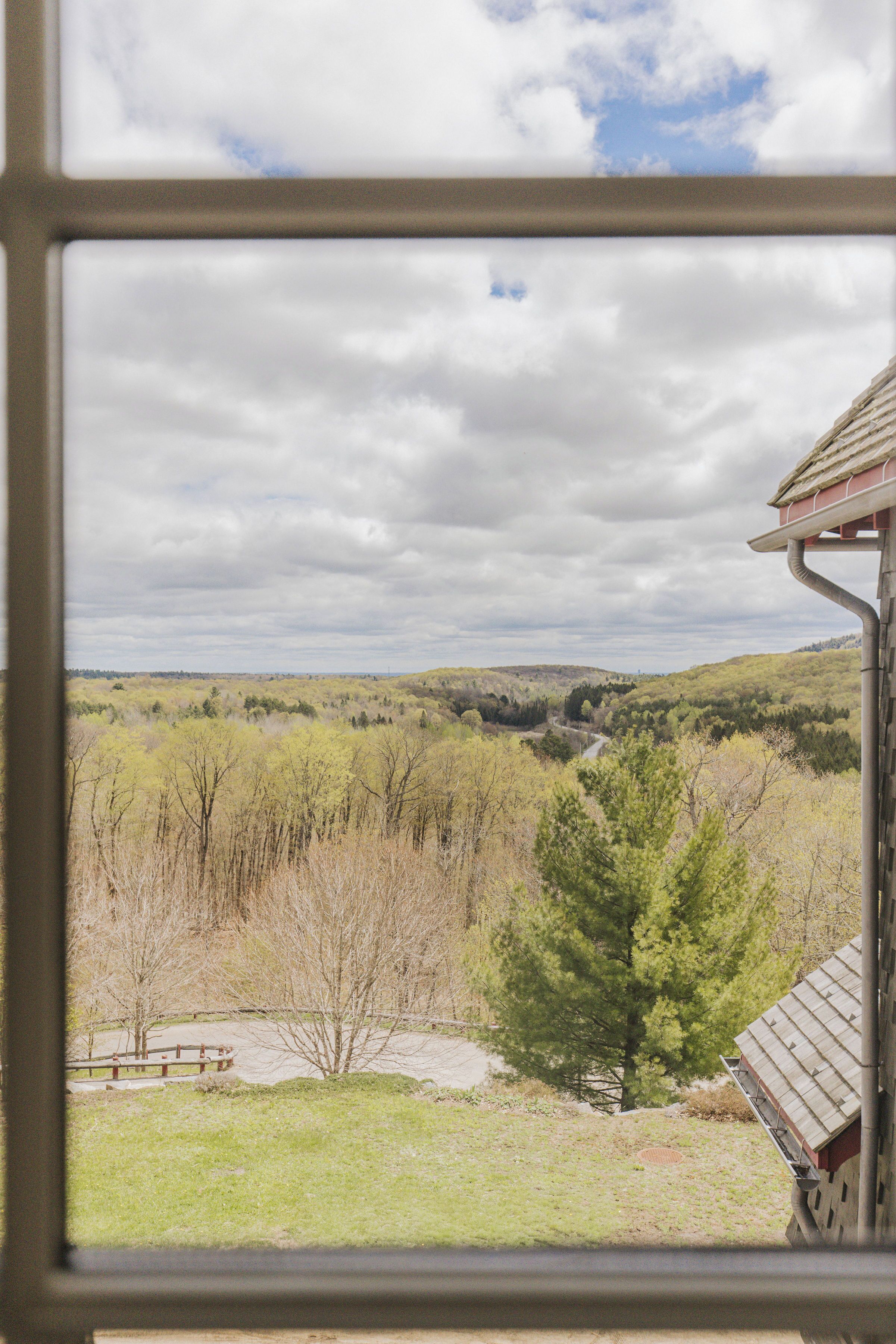 A view through a window of a landscape with a dirt path, trees, and a distant hill.