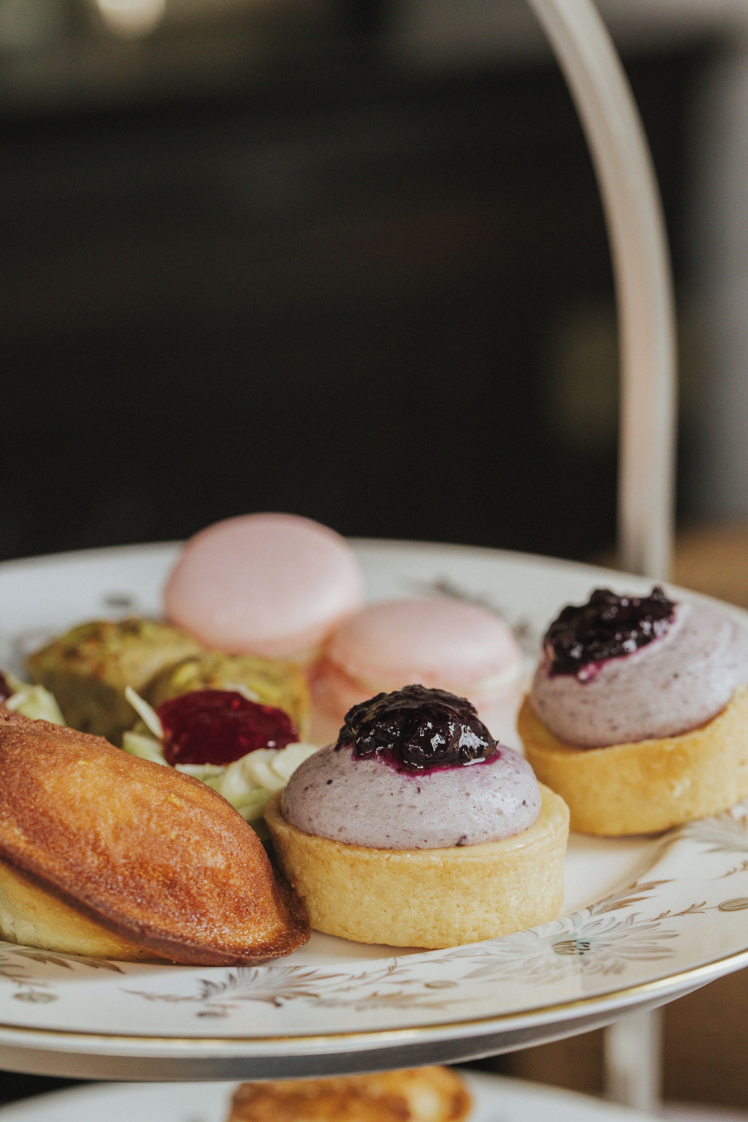Un plato con diversas pastas, incluyendo un macaron rosa, una pasta con arándanos y una pasta dorada.