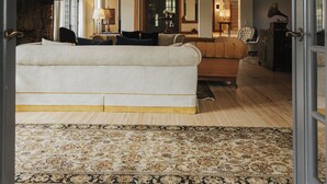 A spacious living room with a large sofa, a patterned rug, and a ceiling with wooden beams.