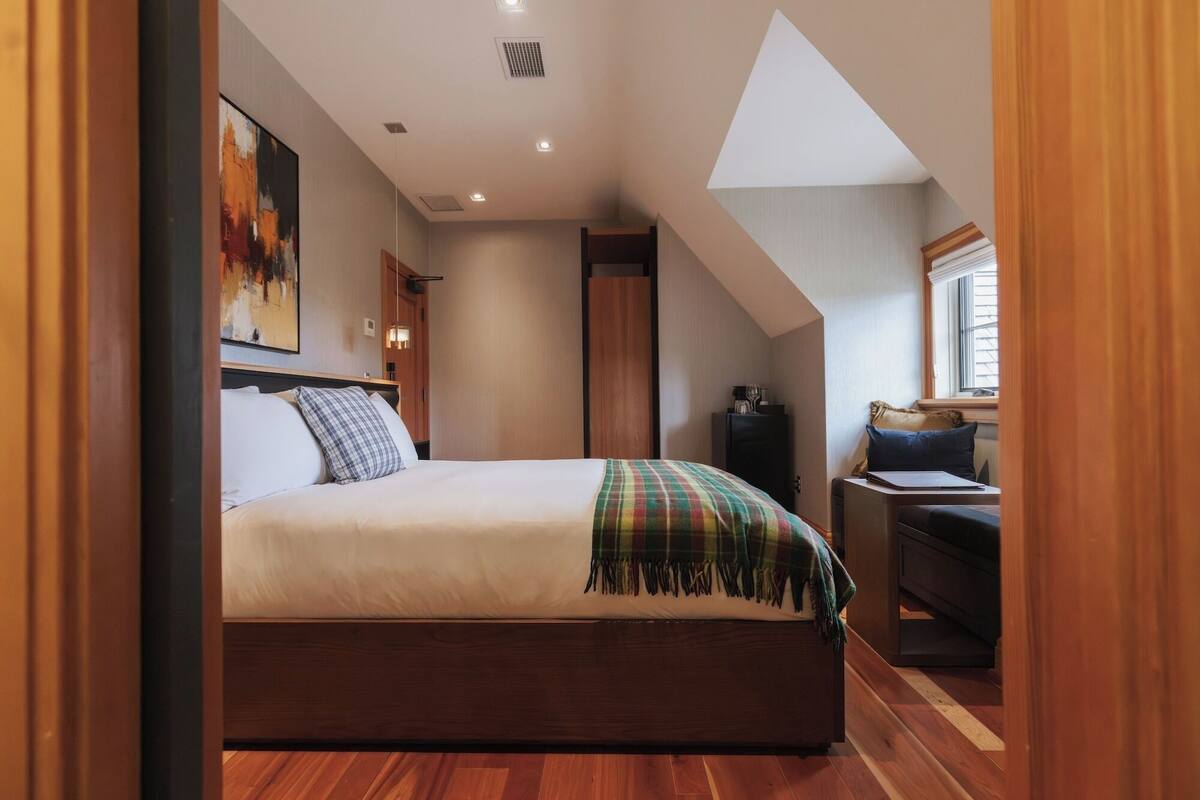 Un dormitorio con cama, escritorio, silla, ventana y un cuadro en la pared.