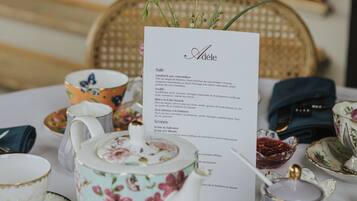 Una mesa dispuesta con tazas de té de estampado floral, una tetera y un menú titulado 'Adele'.