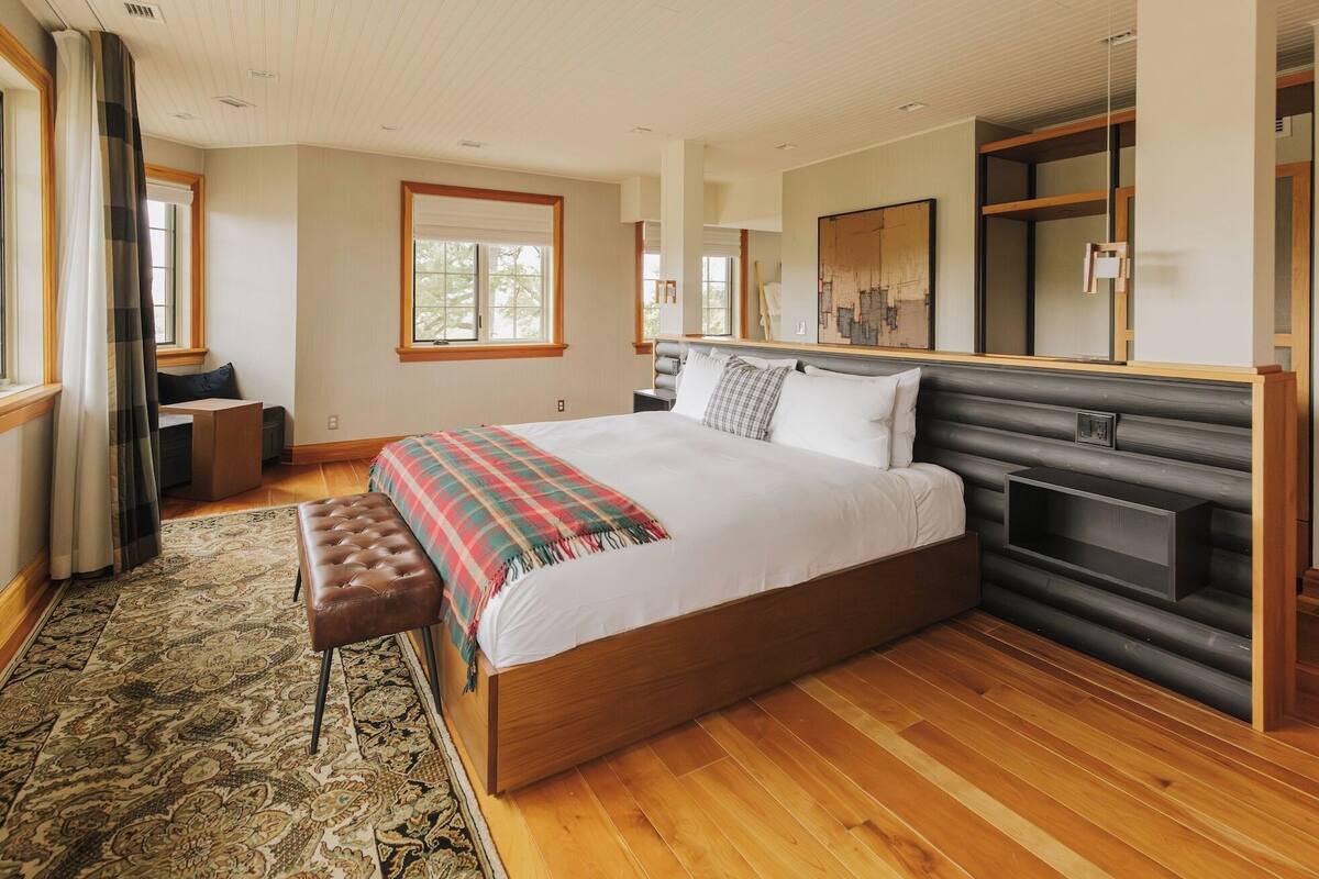 Un dormitorio con una cama grande, un banco de madera, una chimenea y vistas al exterior.