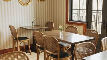 A dining area with striped wallpaper, wooden tables and chairs, and three framed pictures on the wall.