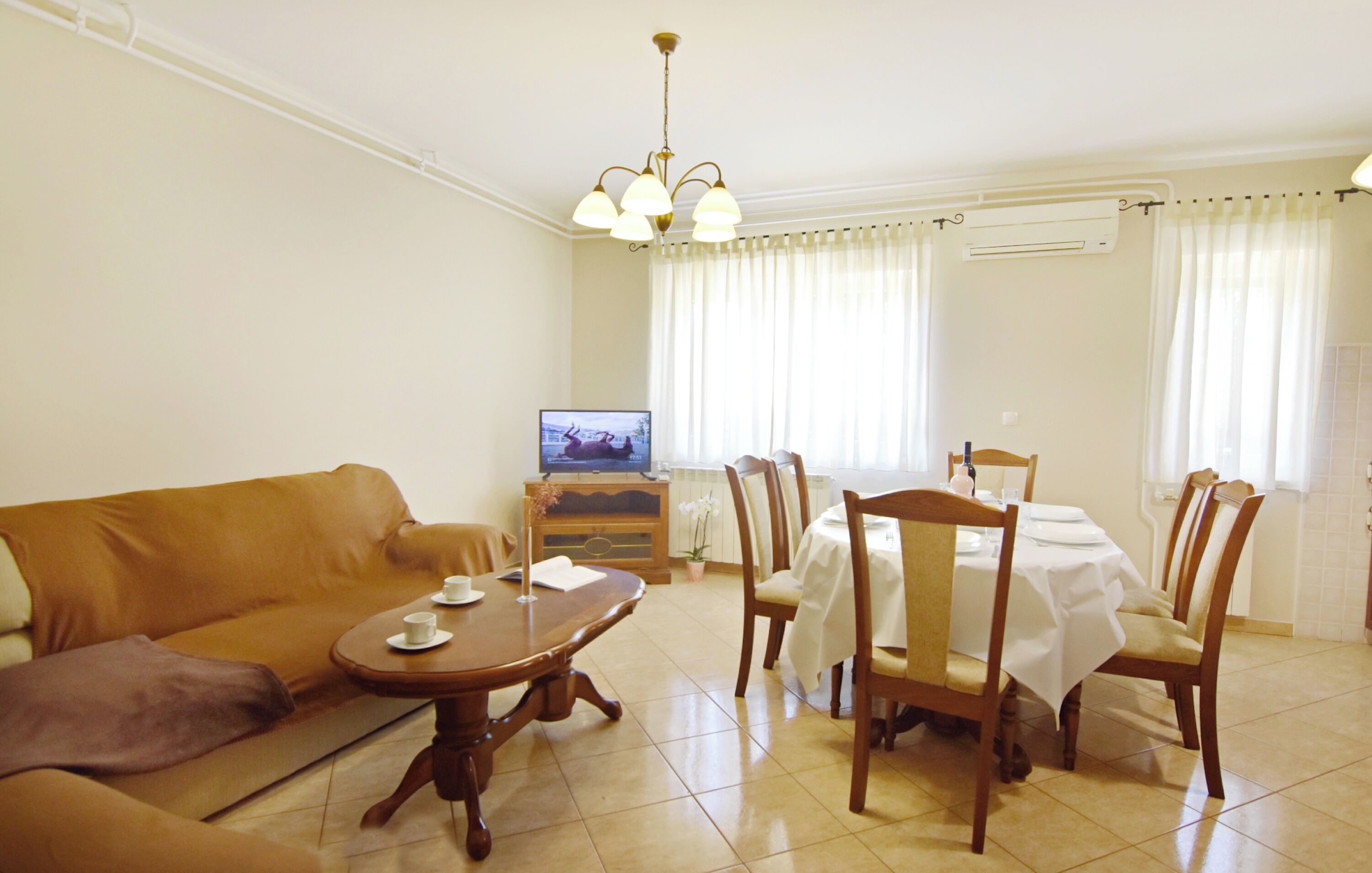 Una sala de estar con sofá, una mesa de comedor con sillas, televisor y radiador.