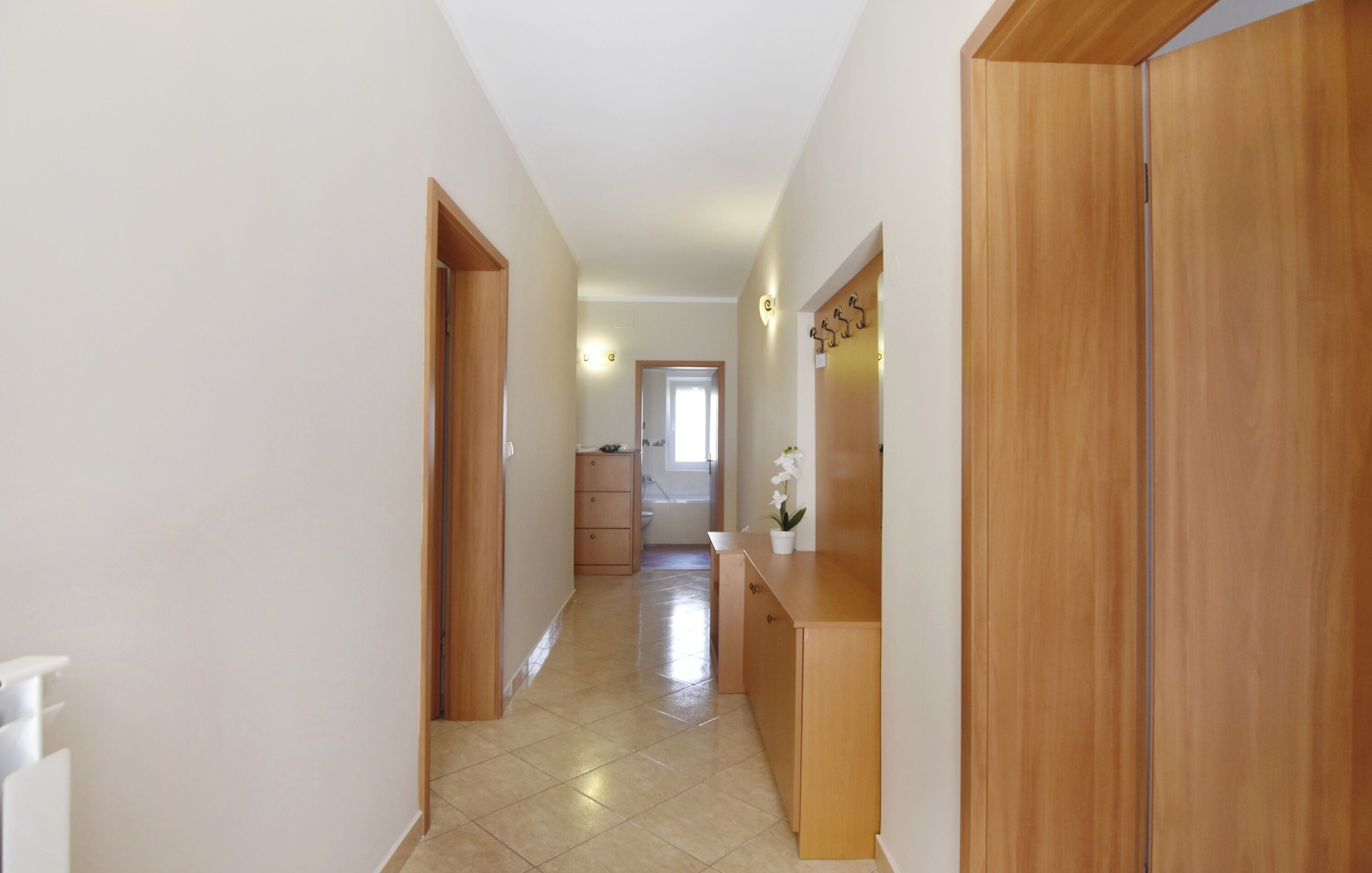 A hallway with wooden doors, a tiled floor, and a small plant on a wooden counter.