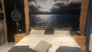 A bedroom with a bed, two nightstands, a wall tapestry, and a door with a circular design. - Villa Lumina Royale With Swimming Pool (Zutendaal)