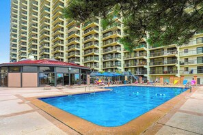 A swimming pool area with a covered seating area, surrounded by high-rise residential buildings. - Stunning Oceanfront Condo with Private Balcony, Pools, Game Room & Beach Access (Ocean City)