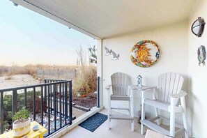 A balcony with a view of the beach, two Adirondack chairs, a small table, and decorative wall art. - Sunny Beach Front Condo w/Beach Access, Private patio, W/D, AC & full kitchen (Ocean City)