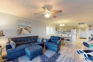 A living room with a sofa, ottoman, and armchair, a ceiling fan, and a dining area with a table and chairs. - Sunny Beach Front Condo w/Beach Access, Private patio, W/D, AC & full kitchen (Ocean City)