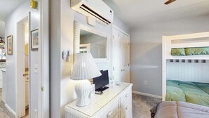 Ein Schlafzimmer mit Etagenbett, Kommode mit Lampe, Spiegel und Klimaanlage.