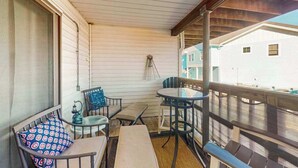 Ein überdachter Balkon mit Holzboden, einem kleinen runden Tisch, einer Bank und einem Stuhl mit gemustertem Sitzkissen.