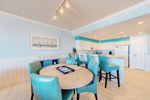 A modern kitchen with white cabinets, a central island, and a dining area with blue chairs. - Ocean's Edge 303 (Ocean City)