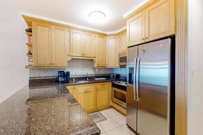 A kitchen with wooden cabinets, a stainless steel refrigerator, a microwave, and a coffee maker. - Spacious Oceanfront - condo on the Boardwalk w/balcony, WiFi, washer/dryer & AC (Ocean City)