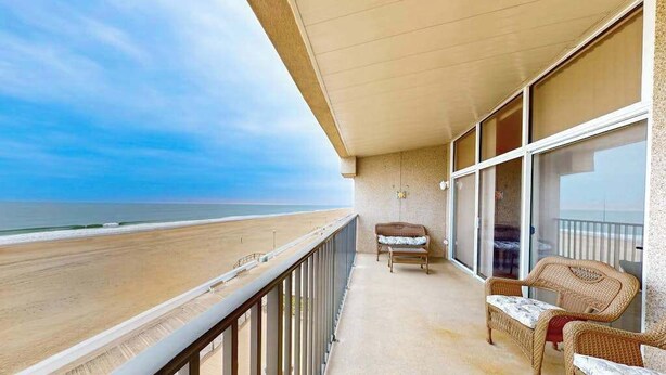 Un balcón con vista a la playa, mobiliario de mimbre y una puerta de cristal.