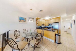 A modern kitchen with wooden cabinets, a stainless steel refrigerator, and a dining area with a glass table and metal chairs. - Spacious Oceanfront - condo on the Boardwalk w/balcony, WiFi, washer/dryer & AC (Ocean City)