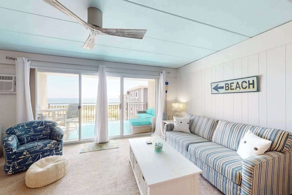 A living room with a sofa, a chair, a coffee table, a ceiling fan, and a sign indicating a beach direction. - Beachloft 3K (Ocean City)