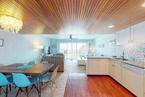 A modern kitchen with white cabinets, a wooden ceiling, and a dining area with blue chairs. - Beachloft 3K (Ocean City)