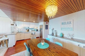 A modern kitchen with white cabinets, a wooden ceiling, and a dining area with a wooden table and chairs. - Beachloft 3K (Ocean City)