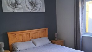 A bedroom with a wooden bed, a nightstand, a lamp, and a large floral painting on the wall.
