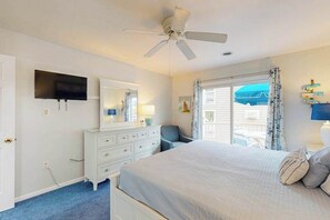 Ein Schlafzimmer mit Bett, Kommode, Fernseher, Deckenventilator und einem Fenster mit Vorhängen.
