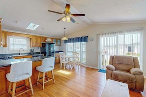 A spacious kitchen with wooden cabinets, a dining area with white chairs, a ceiling fan, and large windows. - Assateague Pointe - Longboat (Berlin)
