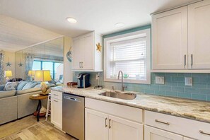 A compact kitchen with a dishwasher, a sink, and a window with blinds. - Sunny oceanfront condo with private balcony, ocean views, free WiFi & AC (Ocean City)