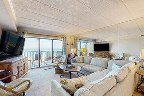 A spacious living room with a large sofa, a television, and a wooden cabinet. - Sunny oceanfront condo with private balcony, ocean views, free WiFi & AC (Ocean City)