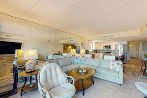 A modern living room with a sectional sofa, a round coffee table, and a TV. - Sunny oceanfront condo with private balcony, ocean views, free WiFi & AC (Ocean City)