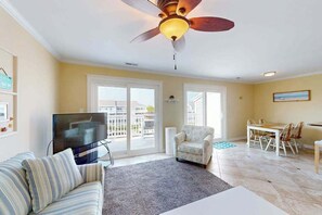 Ein Wohnzimmer mit einer Couch, einem Fernseher, einem Deckenventilator und einem Essbereich mit Tisch und Stühlen.
