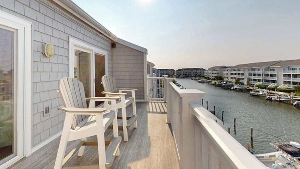 Un balcó amb dues cadires Adirondack, vistes a una marina i un edifici amb façana blanca.