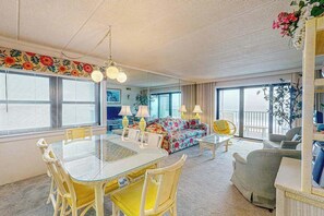 A dining area with a glass table and wicker chairs, a floral sofa, and a yellow armchair. - Waterfront condo w/ocean views, beach access, private balcony, W/D, & Central AC (Ocean City)