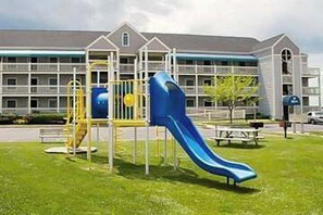 A playground with a slide and climbing structures in front of a building with multiple windows. - Sunny Waterfront Condo w/Canal Views, Balcony, Central AC, Shared Pool & Tennis (Ocean City)