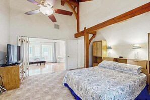 A bedroom with a bed, wooden beams, a ceiling fan, a television, and a door leading to another room. - 13904 Lighthouse Ave (Ocean City)