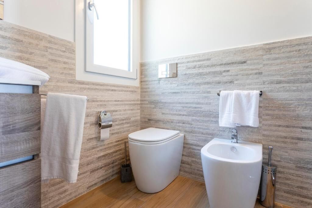 Ein modernes Badezimmer mit Toilette, Waschbecken und Handtuchhalter vor einer strukturierten Wand.