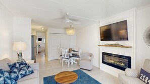 A modern living room with a fireplace, a flat-screen TV, a dining area with white furniture, and a ceiling fan. - Beautiful Ocean view Condo short walk to the beach access (Ocean City)
