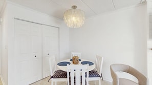 A dining area with a white table, four chairs, a chandelier, and a white door. - Beautiful Ocean view Condo short walk to the beach access (Ocean City)
