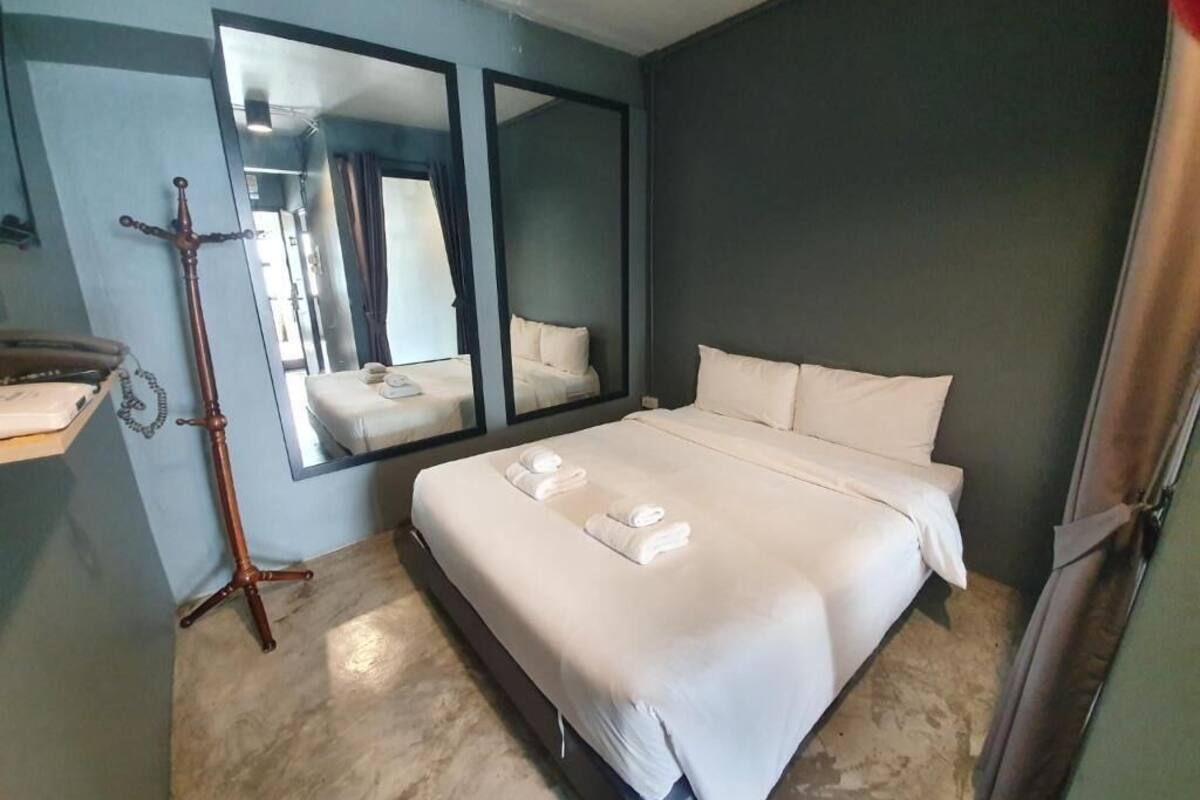 A hotel room with a large bed, a mirror, a wooden stand, and a window.