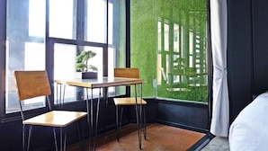 A corner room with a large window, a wooden table, two chairs, and a potted plant.