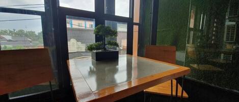 A room with a wooden table and chairs, a potted plant, and large windows with a view of buildings.