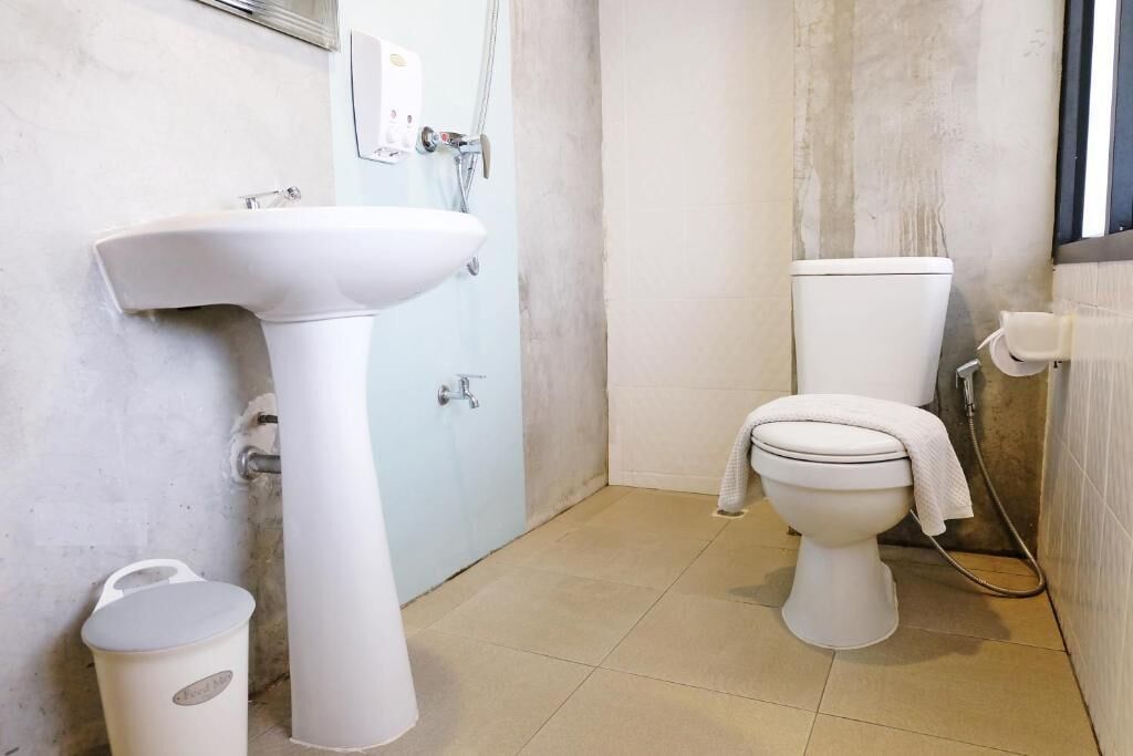 A bathroom with a pedestal sink, toilet, and a small trash bin.