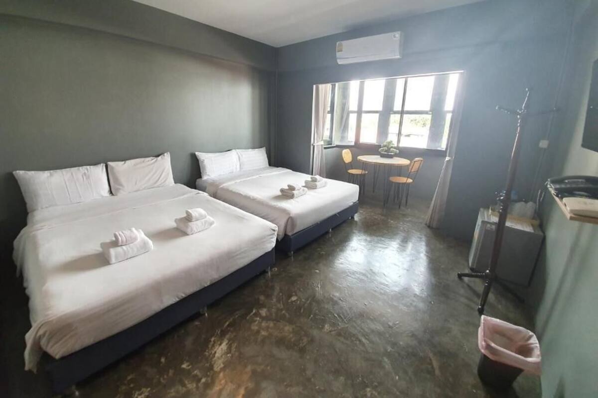 A hotel room with two beds, a small table with chairs, a window, and an air conditioning unit.