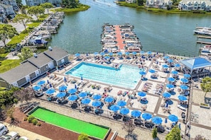 Una piscina con tumbonas y sombrillas, rodeada por un muelle con barcos.